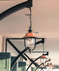 Outdoor pendant lamp hanging with chain from ceiling, featuring vintage style with glass shade under a covered patio.