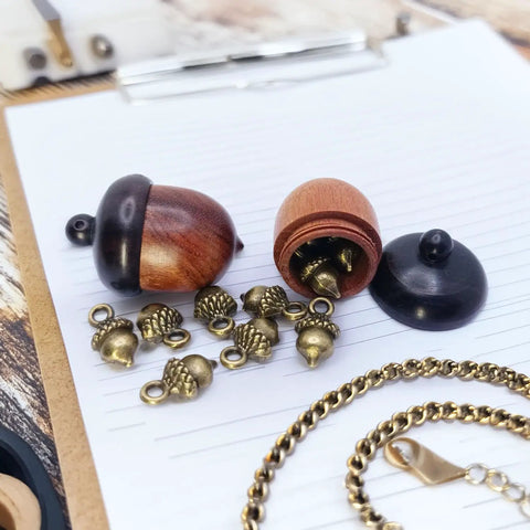 Hella Slick Screw Open Miniature Black Ebony Acorn Curios Set Of Two With Hidden Antique Bronze Pinecones showing acorns and pinecones on paper.