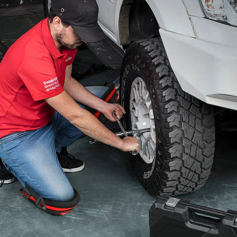 Mechanic using Knee Pads For Work With Soft Gel Core And EVA Foam Padding while fixing a car tire, showcasing ergonomic design.