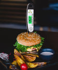 Digital Meat Thermometer For Grilling With Backlit Display, Instant Read In 2 To 4 Seconds inserted in burger on plate