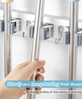 Hand placing mop handle into heavy duty wall mount mop and broom organizer with five slots and four hooks for storage