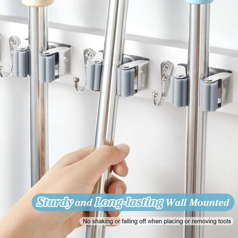 Hand placing mop handle into heavy duty wall mount mop and broom organizer with five slots and four hooks for storage