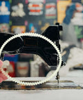 Person holding a rubber drive belt in front of a vintage sewing machine. Beef Up Your Sewing Setup With This 20 Pack Rubber Drive Belts For Sewing Machine Motors Replacement Parts For Household And Industrial Sewing Machines Pedal And Treadle Use Precise Fit Stable Transmission Quiet Operation.