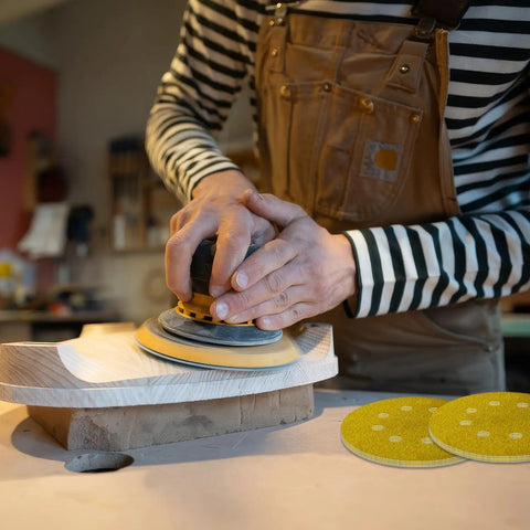 Person using 135 Piece 5 Inch Sanding Discs Set Eight Hole Round Hook And Loop Gold Pro Grade Grit for wood sanding