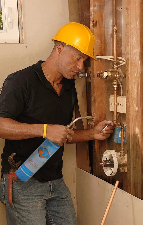 Man soldering pipes using a hand torch with Two 1Lb Empty Propane Tanks for Torch Soldering and Welding in blue
