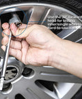 Pencil-style tire pressure gauge with stainless steel stem used to check a car tire valve on a silver alloy wheel
