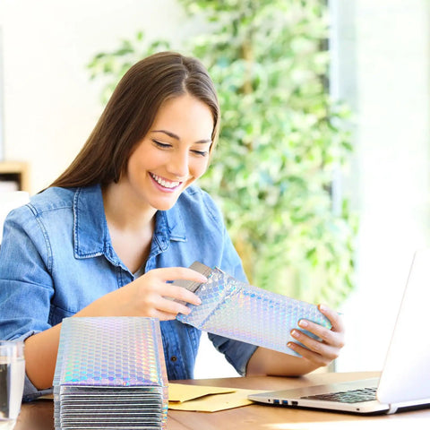 Woman using Dope Rainbow Holographic Bubble Mailers 6 By 9.5 Inch for packaging at desk with laptop, focus keyword in context.