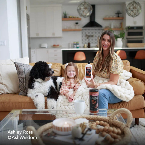A woman holds Top Shelf Leather Cleaner And Conditioner Wipes With Cloth while sitting with a child and dog on a couch.