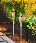 Natural Bamboo Tiki Torch Outdoor Set 2 Pack With Decorative Woven Design For Backyard Vibes And Garden Lighting Outdoor Parties Weddings Festivals Eco Friendly Oil Lamps installed in garden
