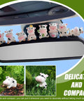 Eight white cow-shaped car dashboard ornaments with black spots perched on a rearview mirror.