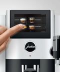 Premium Fully Automatic Chrome Espresso Coffee Machine Featuring A Hella Smooth Four Point Three Inch Smart Touchscreen Display For Twenty Seven Freshly Ground Drinks with user selecting a drink.