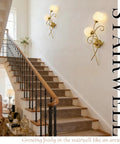 Gold wall sconces set of two illuminate a stairwell with a modern black and brass design, featuring thick clear glass shades.