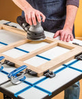 Person using a sander on a wooden frame positioned on Built Legit Aluminum T Track Table Top Measuring Twenty Eight By Forty Inches With Precision T Slots To Lock Clamps.