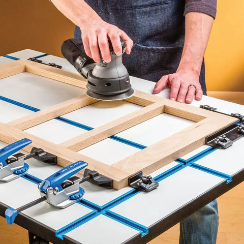 Person using a sander on a wooden frame positioned on Built Legit Aluminum T Track Table Top Measuring Twenty Eight By Forty Inches With Precision T Slots To Lock Clamps.