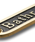 Close-up of a brass bathroom door sign with black finish, similar style to No Soliciting Brass Door Sign For A Chill Home Traditional Style Wall Plaque.