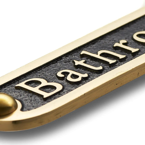 Close-up of a brass bathroom door sign with black finish, similar style to No Soliciting Brass Door Sign For A Chill Home Traditional Style Wall Plaque.