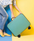 Solid 8 Pack 1.5 Inch Stem Swivel Casters Featuring Strong Locking Brakes For Silky Smooth Roll On Heavy Duty Trash Cans And Utility Carts Quick Swap Universal Dolly Wheels; teal suitcase with black wheels held by a person in blue and yellow background.
