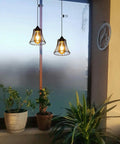 Two Three Pack Battery Operated Outdoor Chandelier Pendant Lights With Rustic Black Metal Bell Shade hanging near indoor plants.