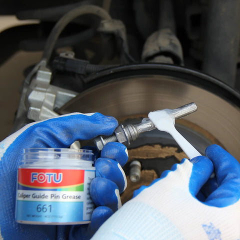 FOTU 661 brake caliper guide pin grease jar being applied to a brake caliper by gloved hands.