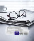 Ultimate Eyeglass Repair Kit Featuring Replaceable Nose Pads And Micro Screwdriver With Assorted Glasses Screws Compact Tool on a table next to glasses and newspaper.