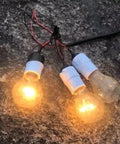 Three clear light bulbs connected by wires, glowing on a rough surface.
