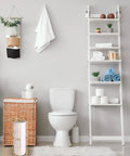 Bathroom setup featuring a modern toilet next to a wicker basket, ladder shelf with decor, and gold finish standing toilet paper holder.