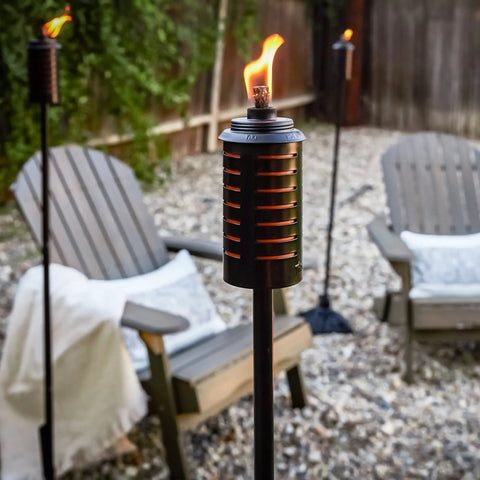 Two Pack 65 Inch Metal Black And Orange Outdoor Torches With Easy Install Lever for Patio with chairs in background