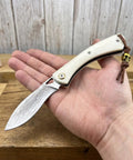 Folding Pocket Knife With 2.99 Inch Damascus Steel Blade And Ivory Synthetic Handle Ultra Portable EDC Knife For Camping And Daily Home Use Built For Everyday Carry And Outdoor Adventures Great Gift For Men, held open in hand, showing blade texture.