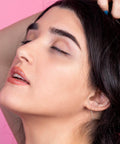 Side view of a person with dark hair, eyes closed, and subtle ear jewelry against a pink background.