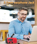 Man using Emergency Weather Radio With AM FM NOAA Reception Hand Crank Power LED Flashlight at a café table with earphones.