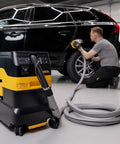Industrial Job Site Dust Extractor Packing Thirty Liters Of Raw Suction And M Class HEPA Filtration in a garage with a worker detailing a car.