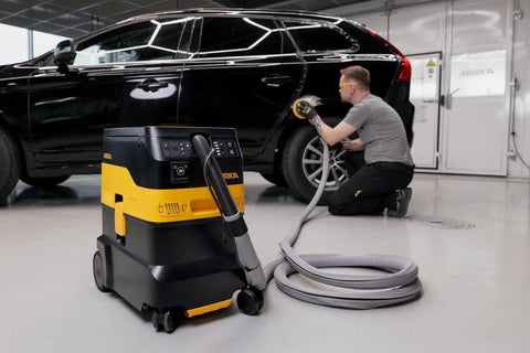 Industrial Job Site Dust Extractor Packing Thirty Liters Of Raw Suction And M Class HEPA Filtration in a garage with a worker detailing a car.