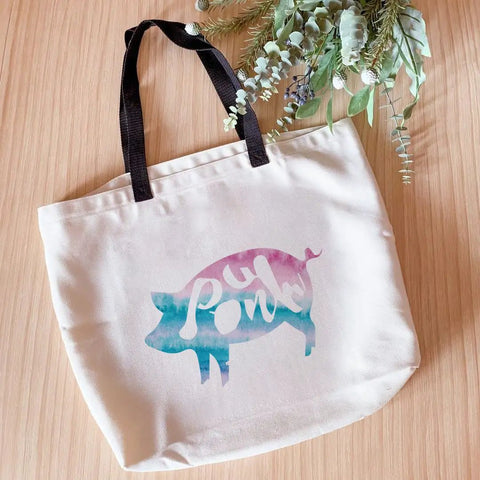 Canvas tote with a colorful pig design on wooden surface with floral decor