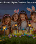 Children playing with baskets and decorative eggs, surrounded by Solar Flickering Flame Outdoor Torch Lights For Garden Decor