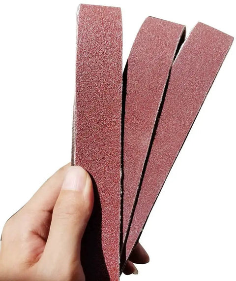 Hand holding 1-1/8 x 21 inch aluminum oxide sanding belts, 3 belts for sanders, from Assorted 1-1/8 Inch By 21 Inch Aluminum Oxide Sanding Belts Set For Most Sanders DIY Pros 18-Pack With 40 80 120 150 240 400 Grits Open Coat Anti Static Moisture Resistant Ideal Replacement Belts