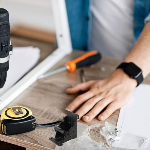 Heavy Duty Black Iron Folding Table Leg Hinges With Spring Two Pack on workbench near tools and person's hand