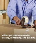 Front view of a gray metal/plastic packing tape dispenser applying 2-inch tape to a cardboard box.