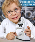Child wearing Ten Pack Kids Disposable Lab Coats White Science Coats With Elastic Knit Cuffs And Front Snap Fasteners posing with microscope.