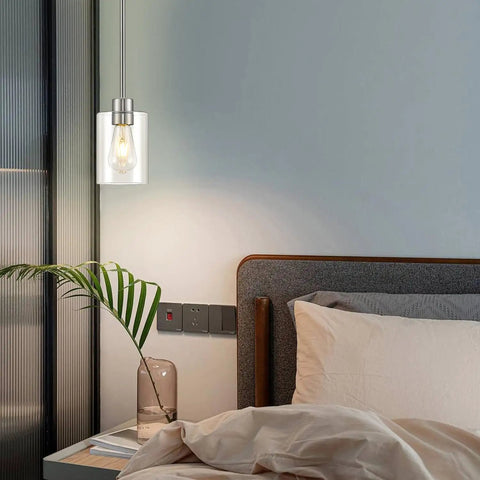 Top Shelf Modern Farmhouse Brushed Nickel Pendant Lights With Clear Glass Shades And Adjustable Rods above a bedside with plant decor.