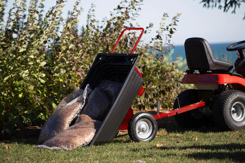 Rock Solid Six Hundred Fifty Pound Poly Dump Cart For Tough Job Site Hauling with bags of debris on grass near a riding lawn mower.