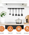 Kitchen with black utensil hanger on tiled wall above stove, displaying four utensils with plant and cutting board beside.