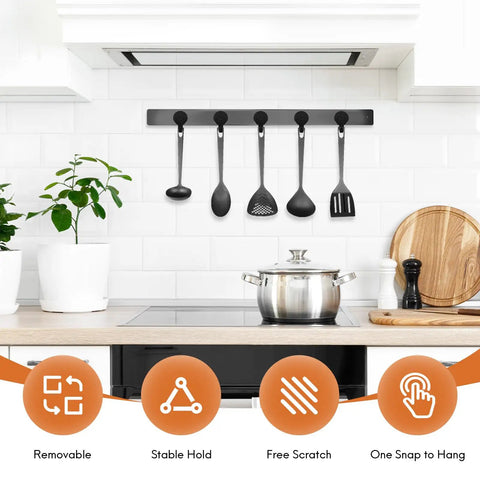 Kitchen with black utensil hanger on tiled wall above stove, displaying four utensils with plant and cutting board beside.