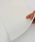 Close-up of white gasket paper sheet, 1/8 inch thick and 7x10 inches, being peeled by hand.