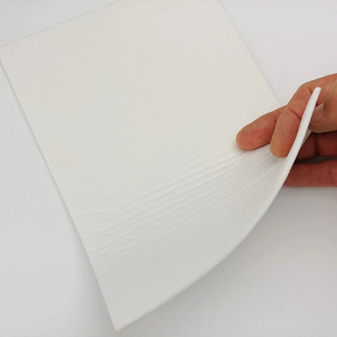 Close-up of white gasket paper sheet, 1/8 inch thick and 7x10 inches, being peeled by hand.