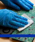 Cleanse 99.9% isopropyl alcohol wipe packet; blue-gloved hands wipe a green circuit board.