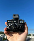 Hand holding Rollei 35 TE film camera with LD Light Meter Pro For Vintage Cameras And Film Photography With One Tap Exposure And Distance Calculator, Ultra Narrow 7 Degree Spot Meter, Built In Laser Rangefinder, Pocket Size All In One Meter For Fast Accurate Shots On The Go No Guesswork