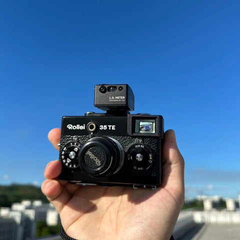 Hand holding Rollei 35 TE film camera with LD Light Meter Pro For Vintage Cameras And Film Photography With One Tap Exposure And Distance Calculator, Ultra Narrow 7 Degree Spot Meter, Built In Laser Rangefinder, Pocket Size All In One Meter For Fast Accurate Shots On The Go No Guesswork