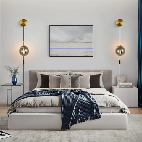 Set Of 2 Plug-In Wall Sconces With Brushed Brass Finish And Smoke Grey Glass Globes mounted above a modern bed.