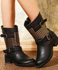Black leather mid-calf boots, side view, with bronze pyramid studs on the shaft and buckled straps