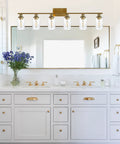Modern bathroom with gold fixture, wide mirror, and elegant white vanity with decorative hardware and floral accent
